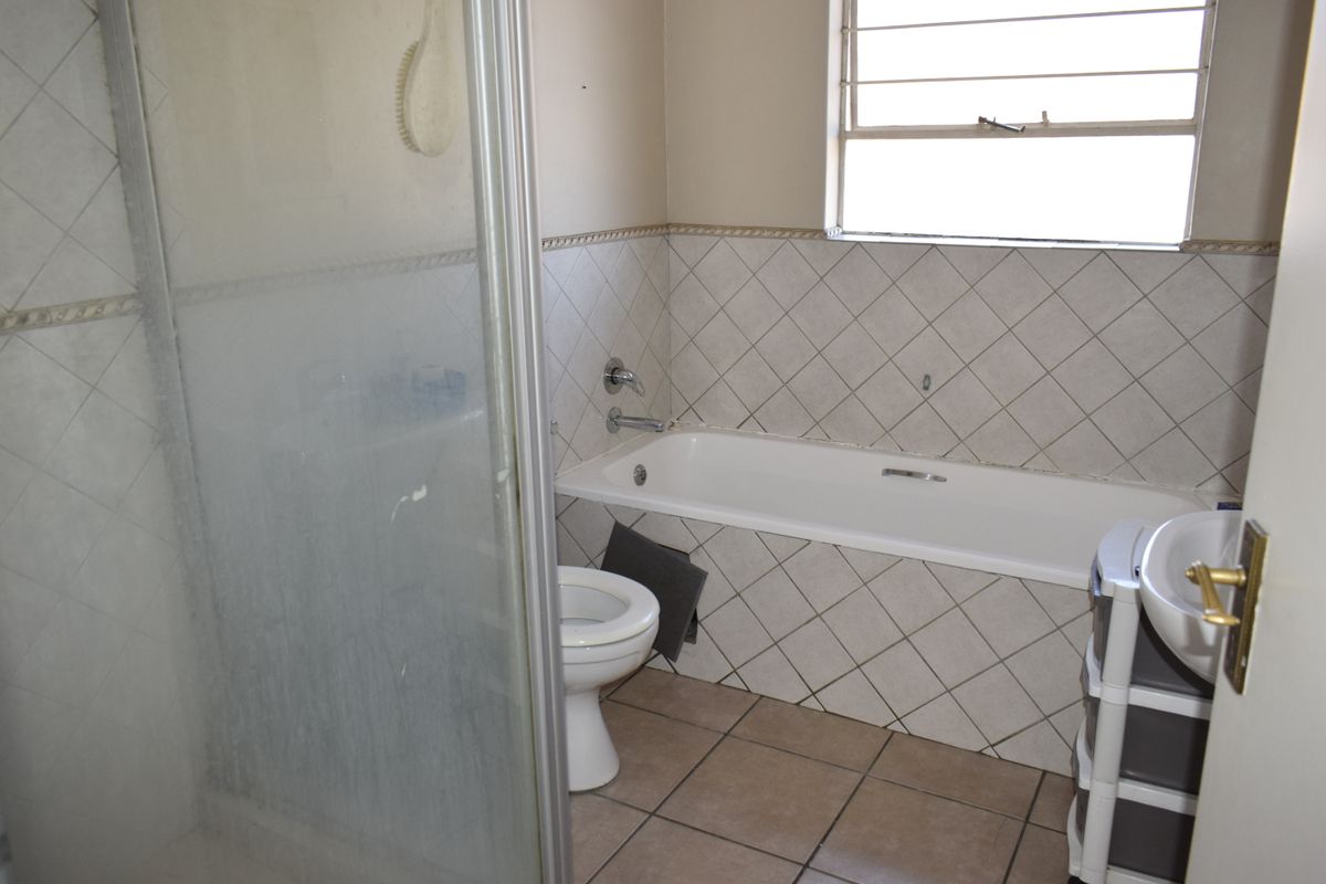 A dated bathroom featuring a shower enclosure, bathtub, toilet, and washbasin with tiled finishes throughout.