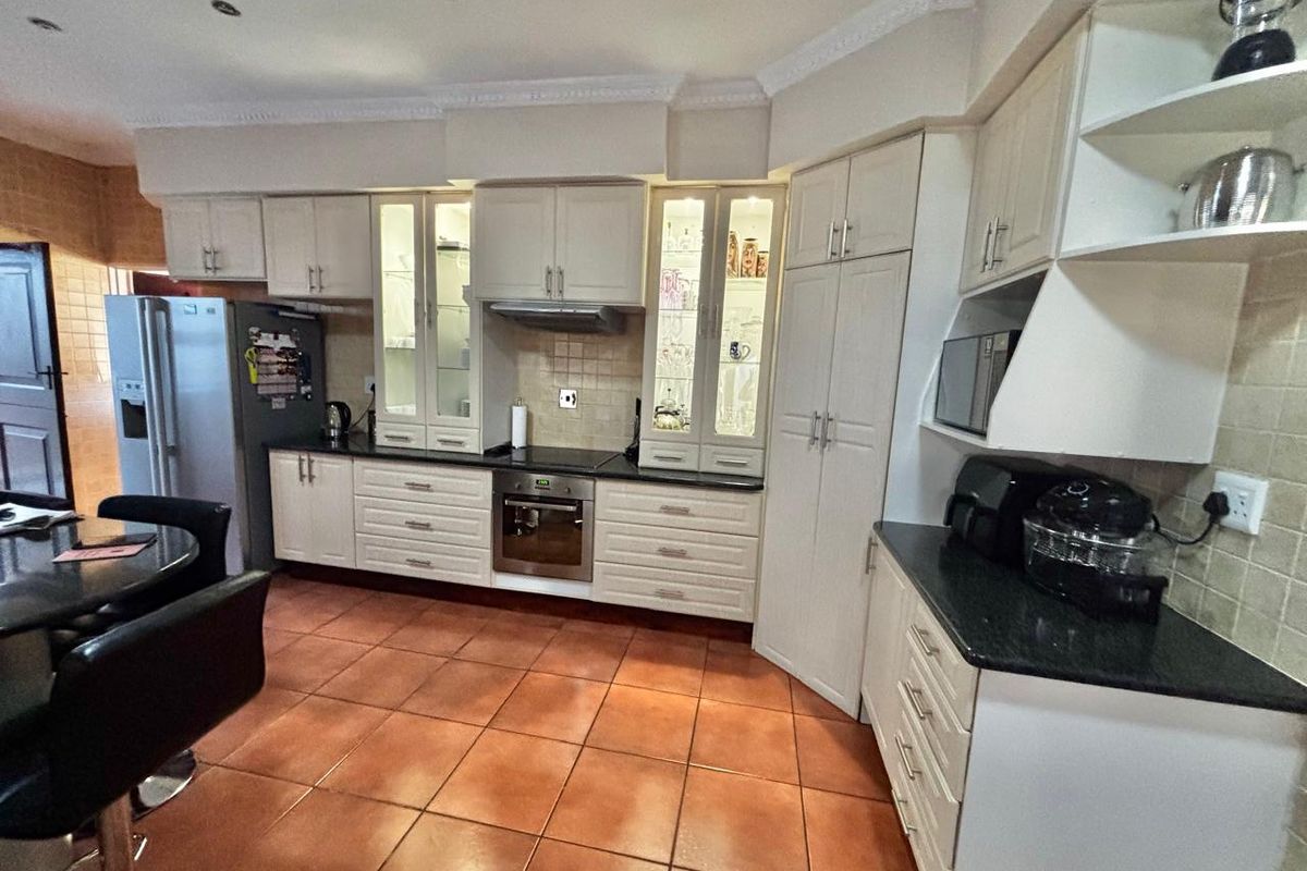 A functional kitchen featuring white cabinetry, dark granite countertops, tiled flooring, and built-in oven and extractor fan.