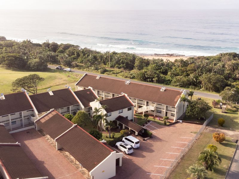 Aerial view of a residential flat complex featuring tiled roofs, paved parking areas, and proximity to the coastline.