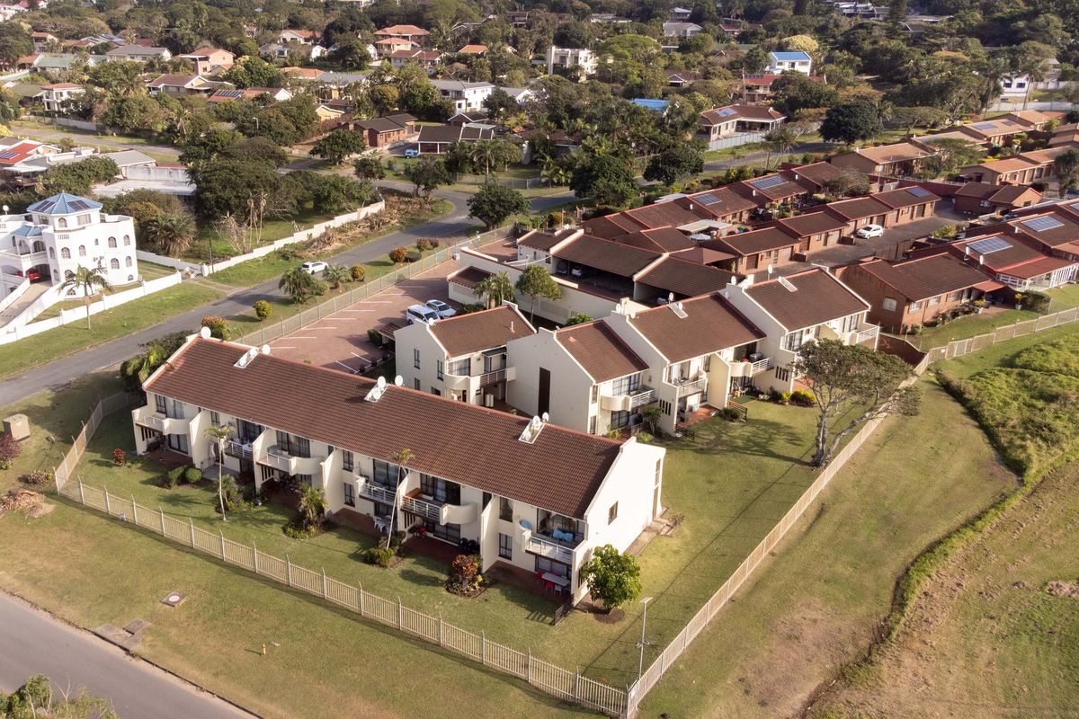 Aerial view of a residential flat complex featuring tiled roofs, communal garden spaces, and paved parking areas within a suburban neighborhood.