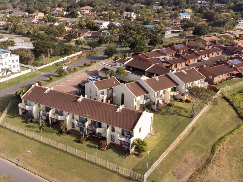 Aerial view of a residential flat complex featuring tiled roofs, communal garden spaces, and paved parking areas within a suburban neighborhood.