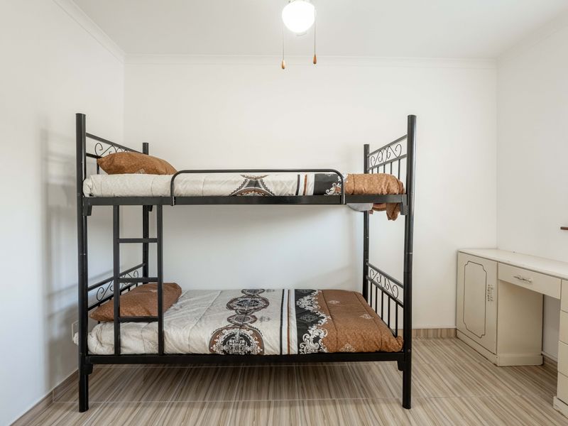 A functional bedroom featuring tiled flooring, a built-in vanity unit, and a window with venetian blinds.