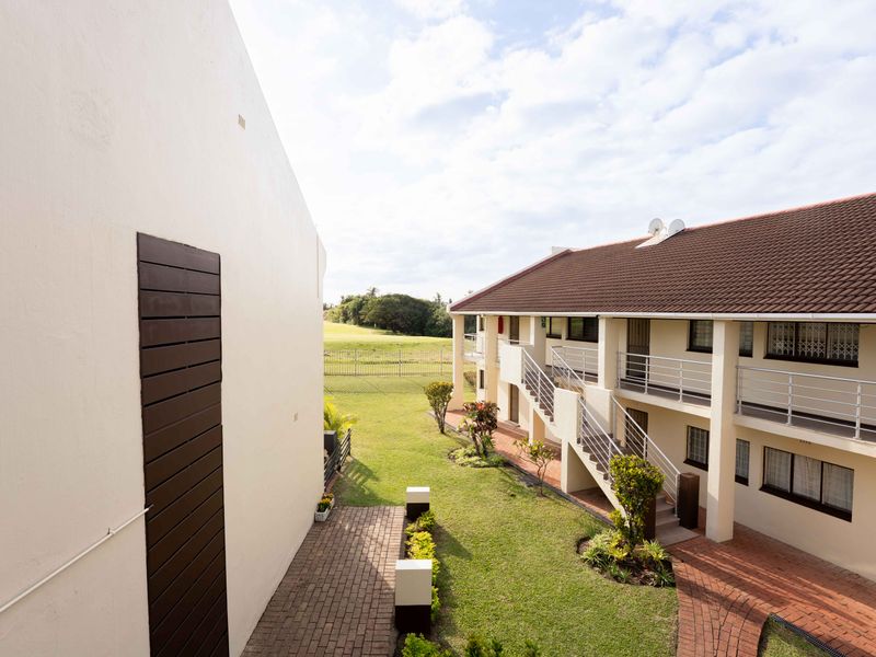 View of the rear exterior of the flat complex, featuring a communal garden, paved walkways, and external staircases leading to upper-level units.