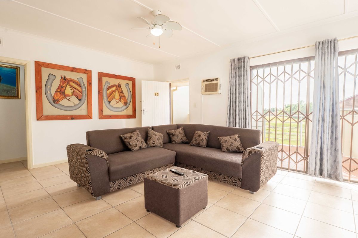A bright living room featuring tiled flooring, a ceiling fan, a wall-mounted air conditioner, and a sliding glass door with a security gate.