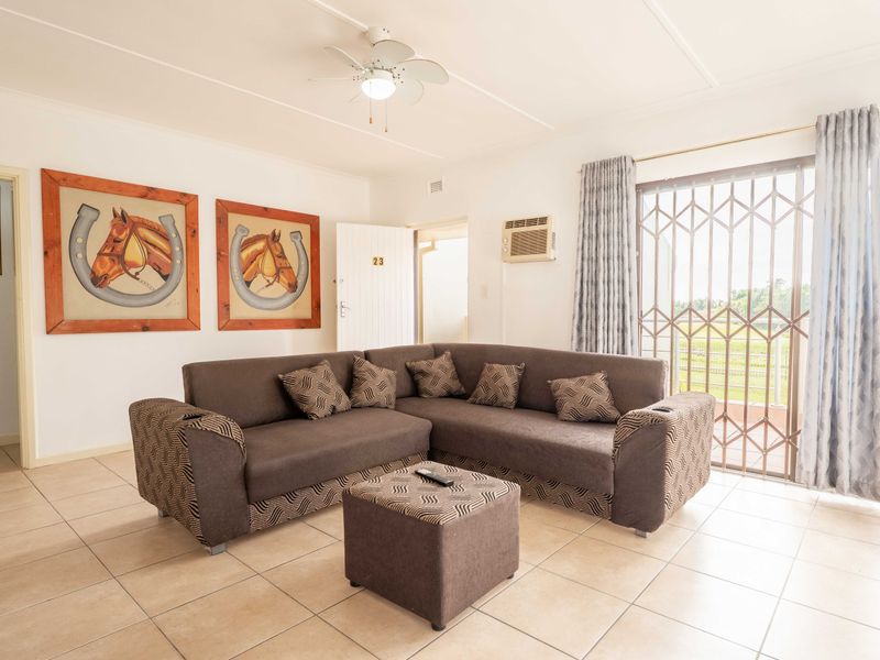 A bright living room featuring tiled flooring, a ceiling fan, a wall-mounted air conditioner, and a sliding glass door with a security gate.