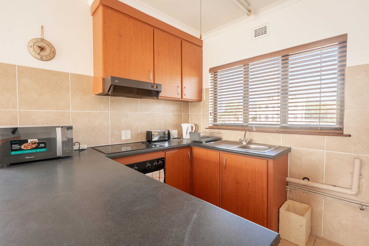 A functional kitchen featuring wood-look cabinetry, dark laminate countertops, a built-in hob and oven, and a tiled splashback with a window for natural light.