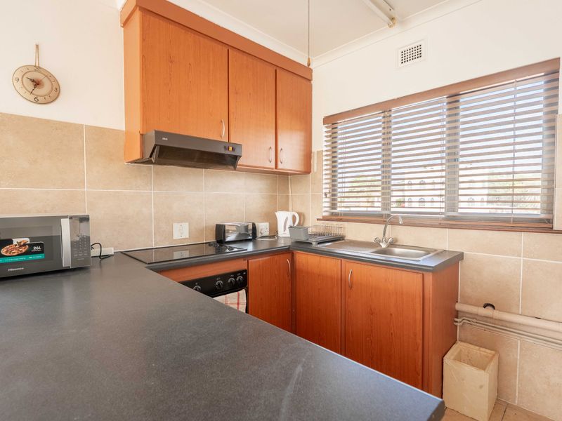 A functional kitchen featuring wood-look cabinetry, dark laminate countertops, a built-in hob and oven, and a tiled splashback with a window for natural light.