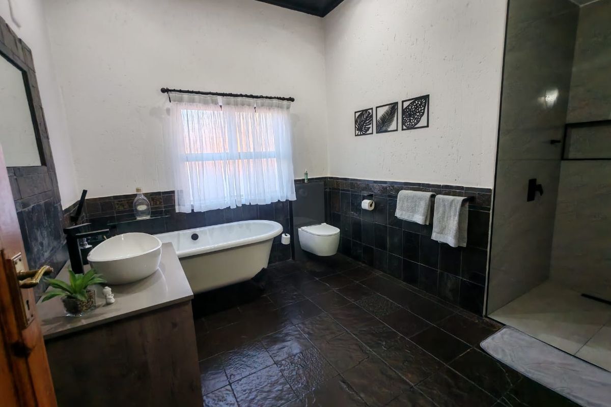 Modern bathroom featuring a freestanding bathtub, wall-mounted toilet, walk-in shower, and a vanity with a vessel sink, finished with dark tiled flooring and walls.
