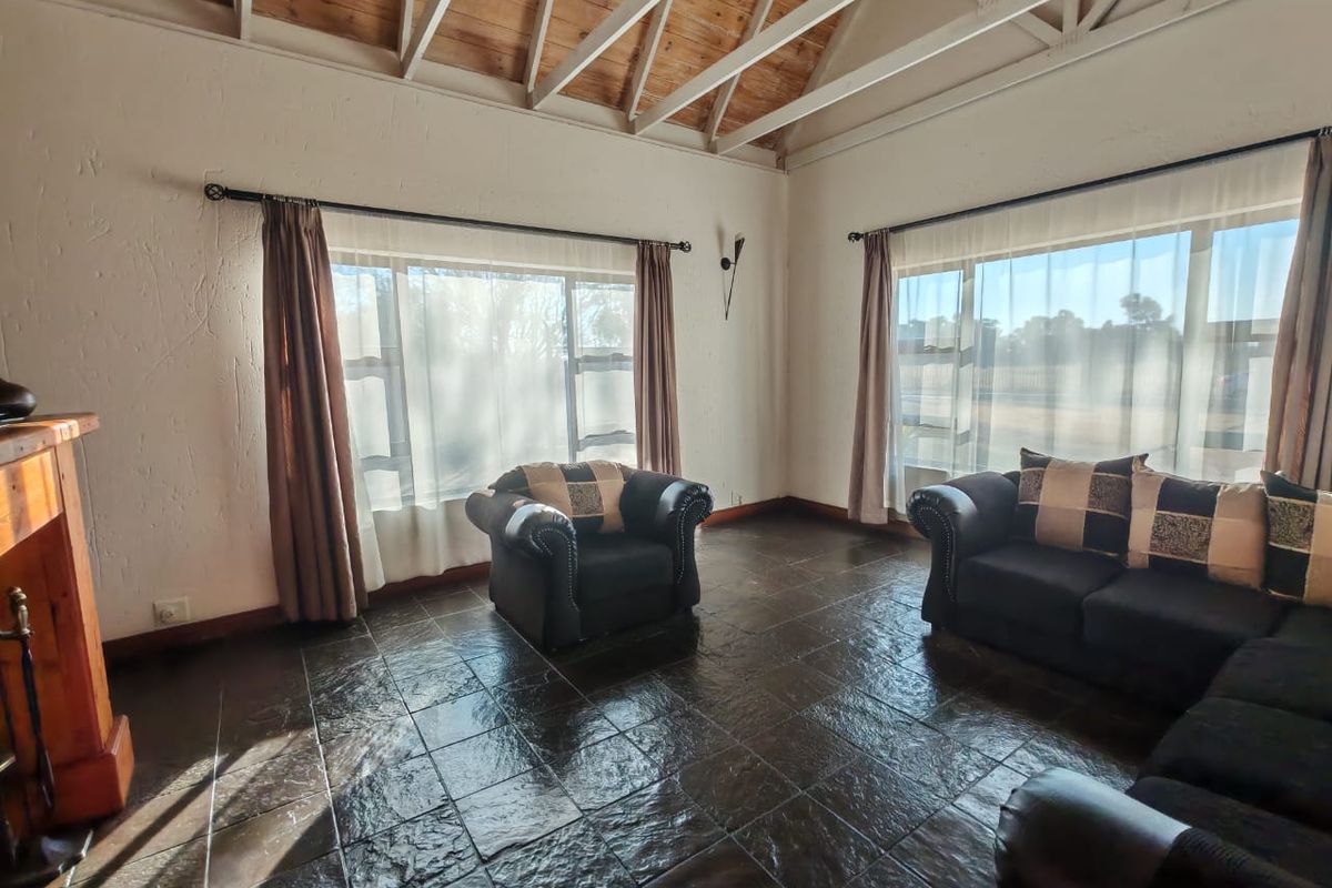 Spacious living room featuring exposed timber ceiling beams, dark tiled flooring, and a fireplace, offering a rustic and inviting atmosphere.