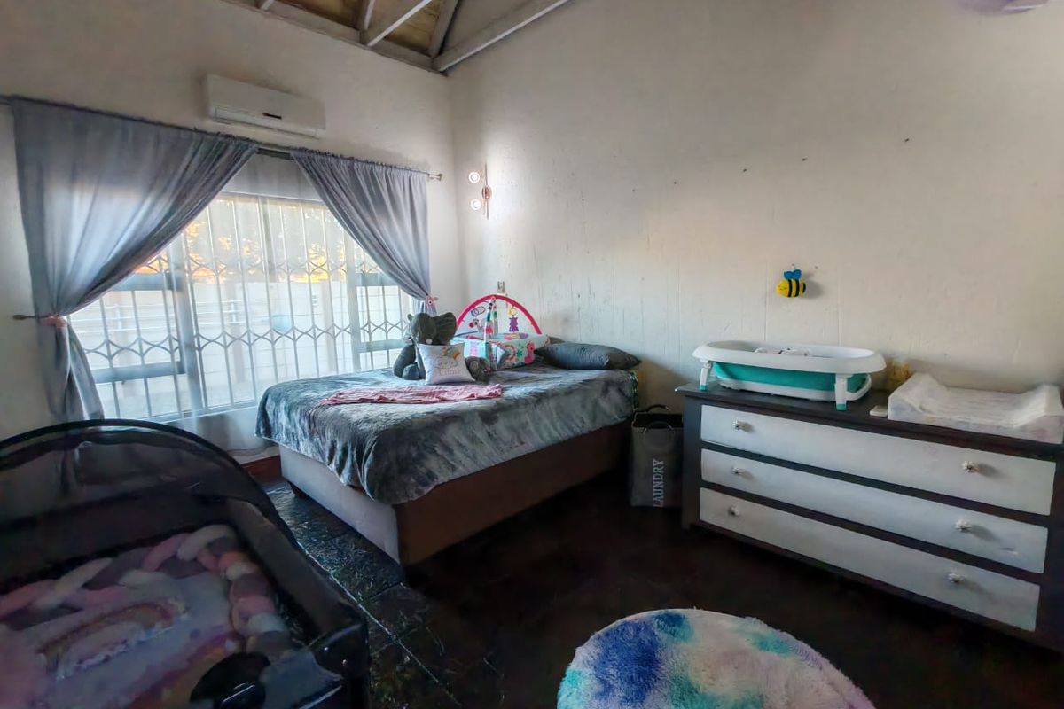 A bedroom featuring exposed timber rafters, tiled flooring, and a wall-mounted air conditioning unit, offering a functional space with potential for cosmetic updates.