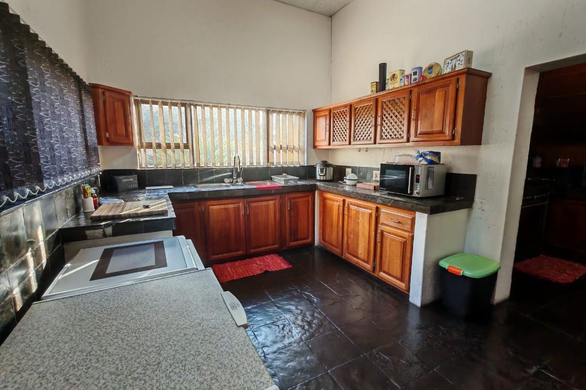 A functional kitchen featuring wooden cabinetry, tiled countertops, and a double sink, offering a dated aesthetic with potential for modern renovation.