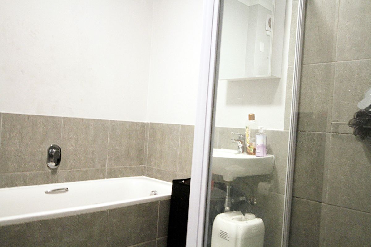 A functional bathroom featuring a bathtub with wall-mounted mixer, a pedestal basin, and a glass-enclosed shower area with neutral wall tiling.