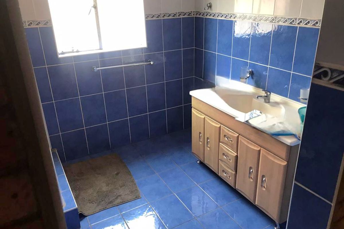 A bathroom featuring blue wall and floor tiles, a wooden vanity cabinet with an integrated sink, and a window for natural light.