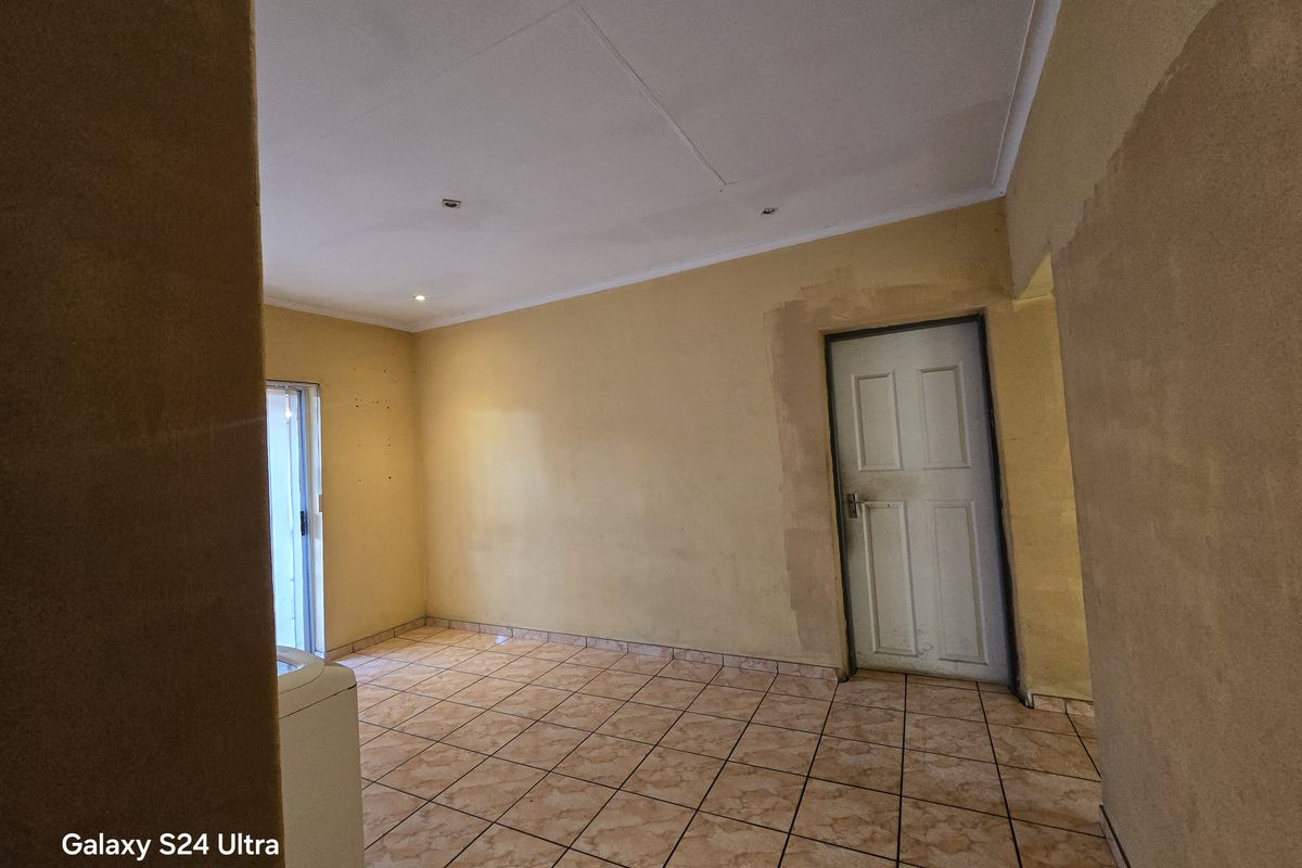 An empty living area featuring ceramic floor tiles, recessed lighting, and unfinished wall surfaces, offering a blank canvas for renovation and interior design.