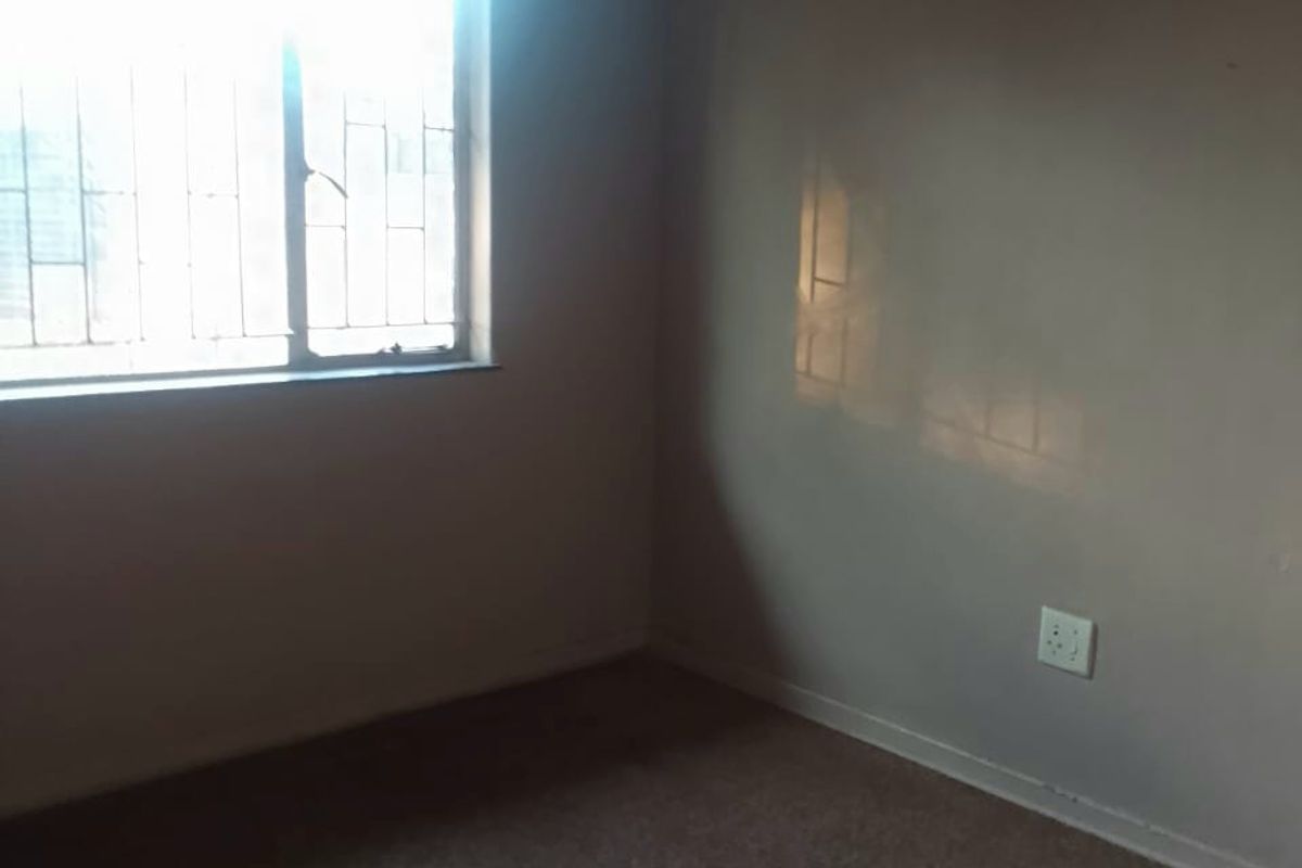 An empty bedroom featuring carpeted flooring, a window with security bars, and neutral wall finishes, offering a blank canvas for personalization.
