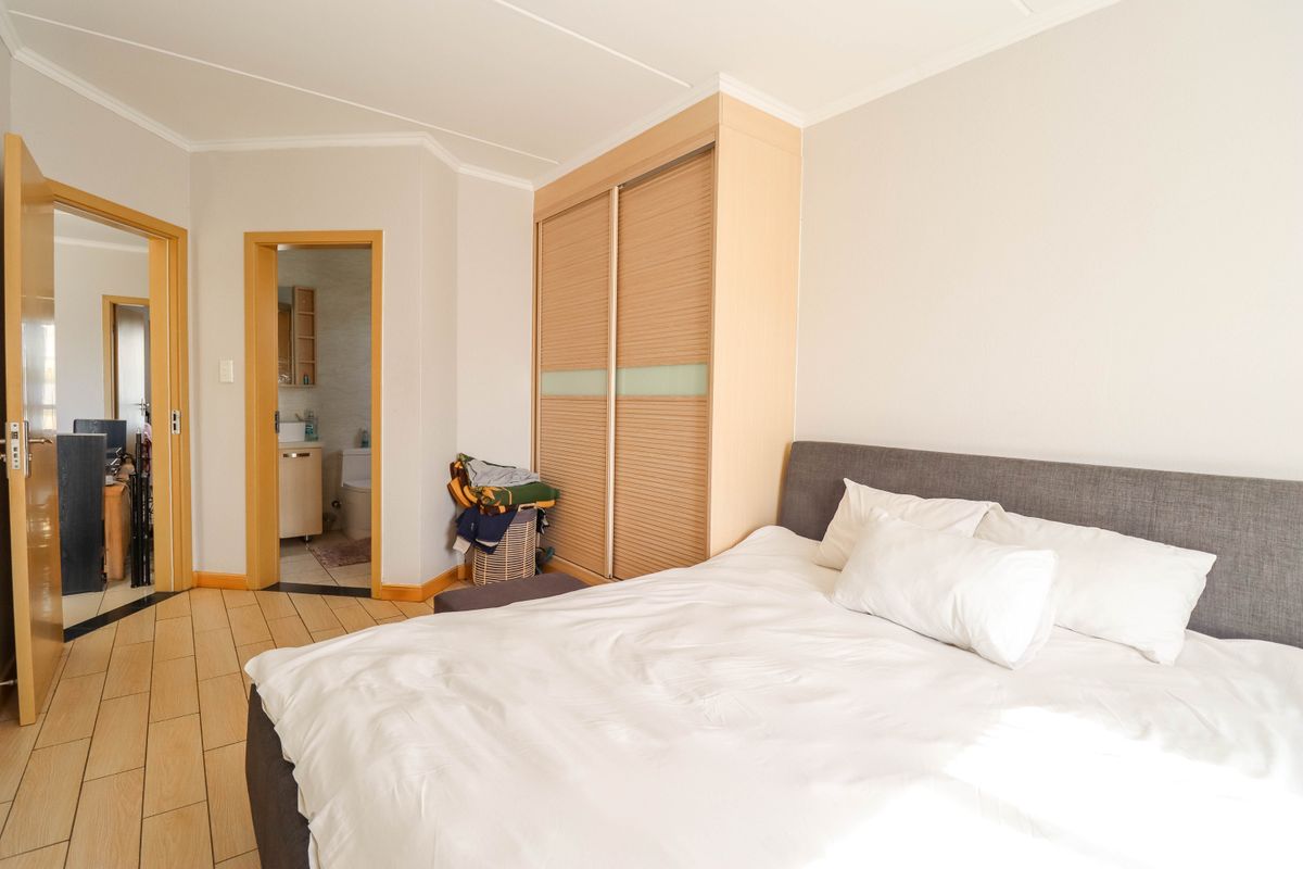 A well-lit bedroom featuring built-in wooden sliding door cupboards and direct access to an en-suite bathroom with tiled flooring throughout.
