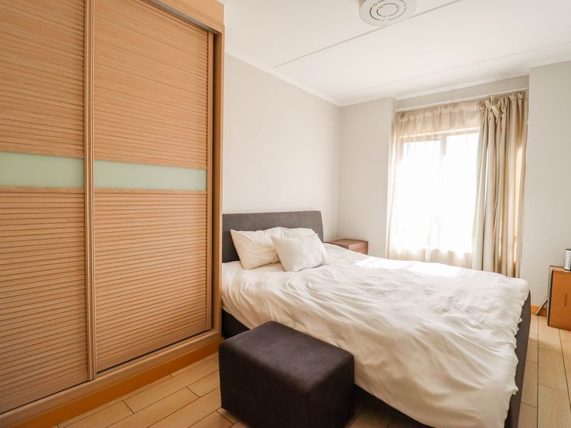 A well-lit bedroom featuring built-in sliding door wardrobes and light-toned wood-look flooring, providing a clean and functional living space.