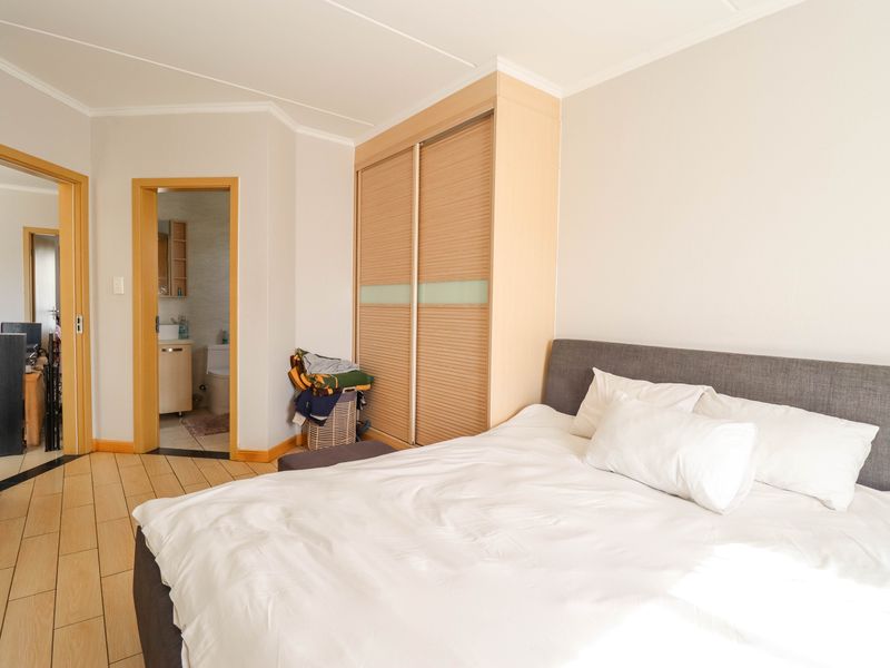 A well-lit bedroom featuring built-in wooden sliding door cupboards and direct access to an en-suite bathroom with tiled flooring throughout.