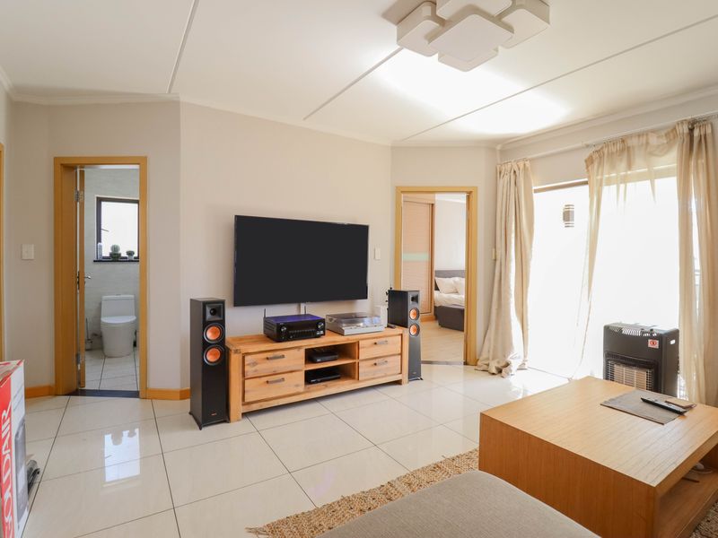 A bright living room featuring tiled flooring, neutral walls, and direct access to adjacent rooms and a balcony area.