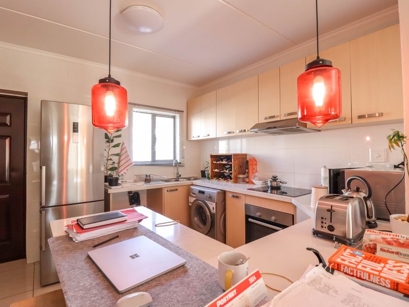 A functional kitchen featuring light wood cabinetry, integrated oven, hob, extractor fan, and built-in laundry appliance space with tiled splashbacks.