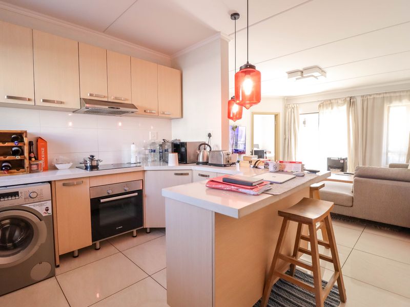 Open-plan kitchen featuring light wood cabinetry, integrated oven, hob, extractor fan, and a breakfast counter, seamlessly flowing into the adjacent living area.