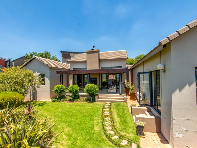 Rear view of the property featuring a landscaped garden, paved pathway, and a covered patio area with a timber pergola and external chimney.