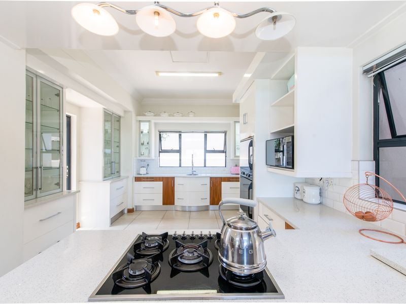 A bright, modern kitchen featuring quartz countertops, a gas hob, built-in oven, and ample glass-fronted cabinetry with a clean, contemporary finish.