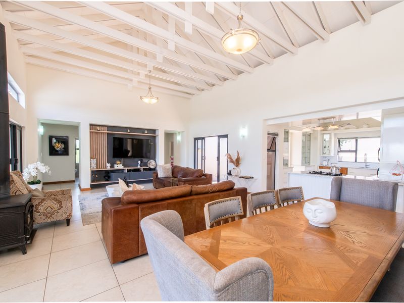 Spacious open-plan living and dining area featuring a vaulted exposed beam ceiling, a cozy wood-burning fireplace, and a modern integrated kitchen.