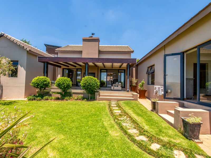 A well-maintained rear exterior featuring a covered patio with a timber pergola, masonry chimney, and a landscaped garden with a stone pathway.