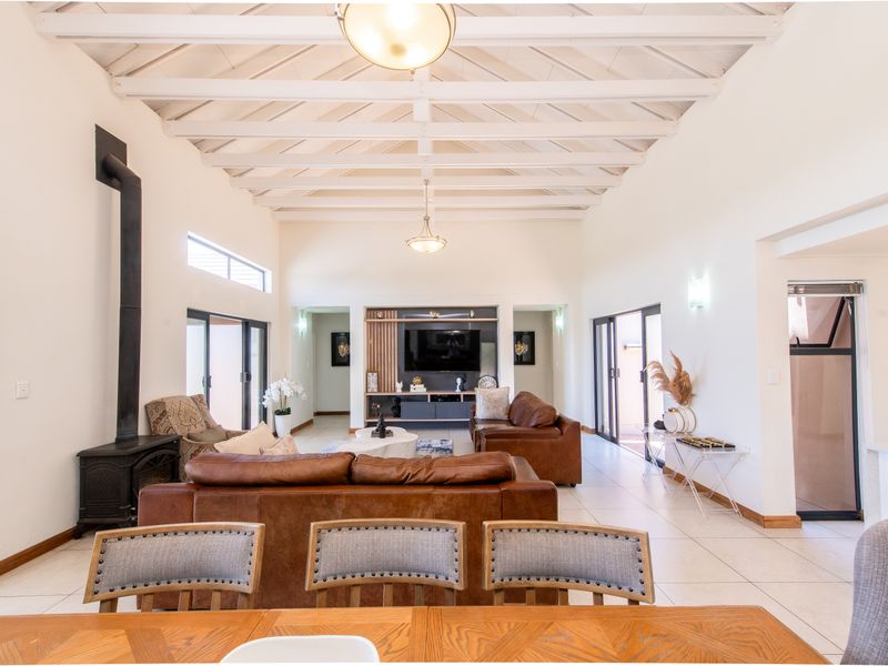 Spacious open-plan living area featuring high exposed timber ceilings, a modern wood-burning fireplace, and seamless access to outdoor spaces through sliding glass doors.