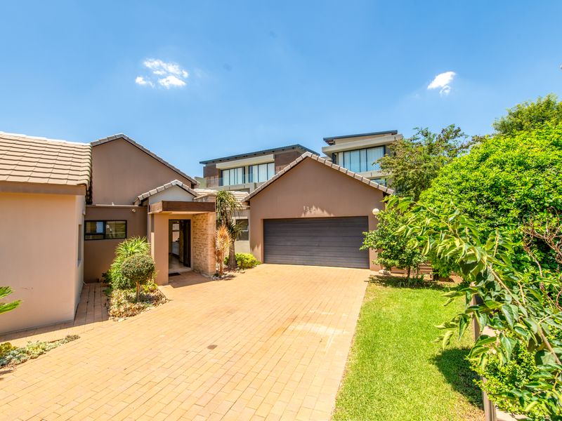 Front elevation of a modern residence featuring a paved driveway, double garage, and well-maintained garden with stone cladding accents.