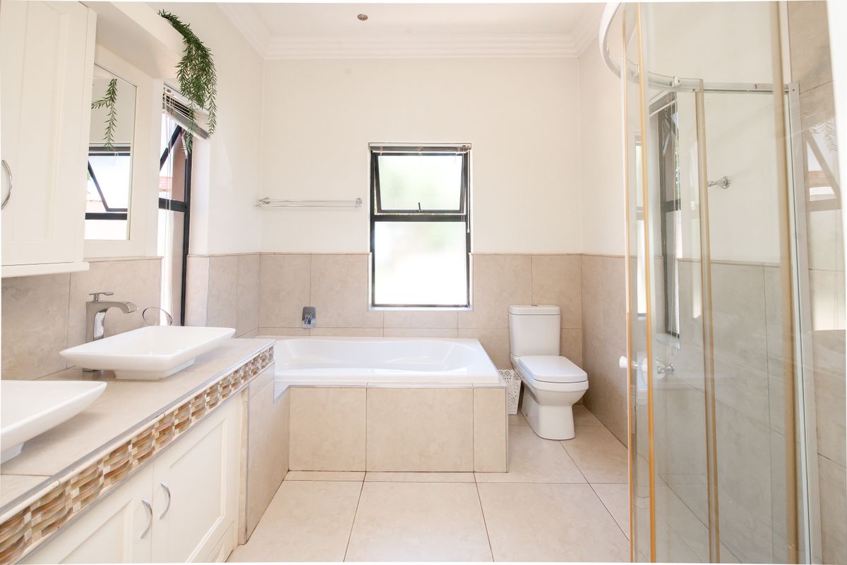 A bright, modern bathroom featuring a double vanity with vessel sinks, a built-in bathtub, a separate shower enclosure, and neutral floor-to-ceiling tiling.