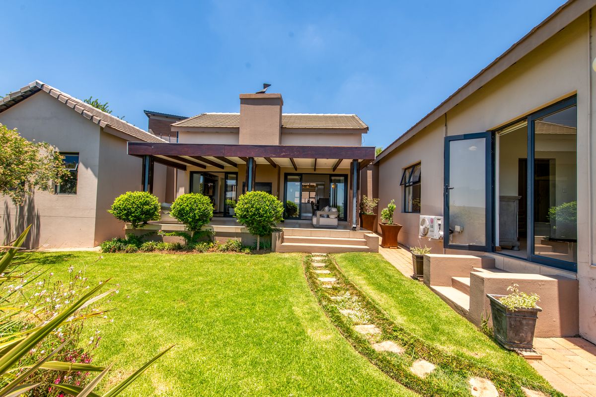 A well-maintained rear exterior featuring a covered patio with a timber pergola, masonry chimney, and a landscaped garden with a stone pathway.