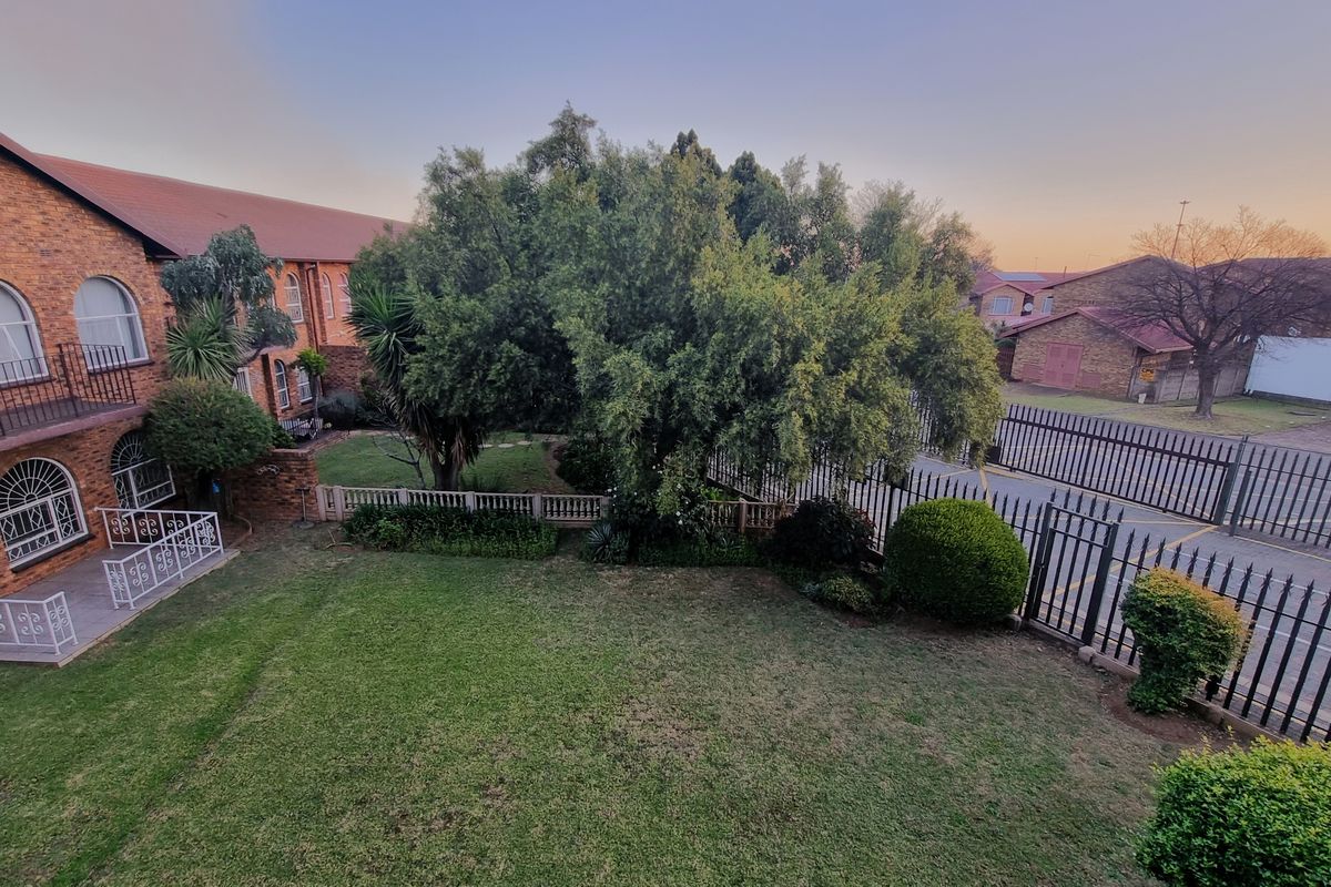 An elevated view of a townhouse complex featuring a well-maintained garden, brick facade, and secure wrought iron fencing.