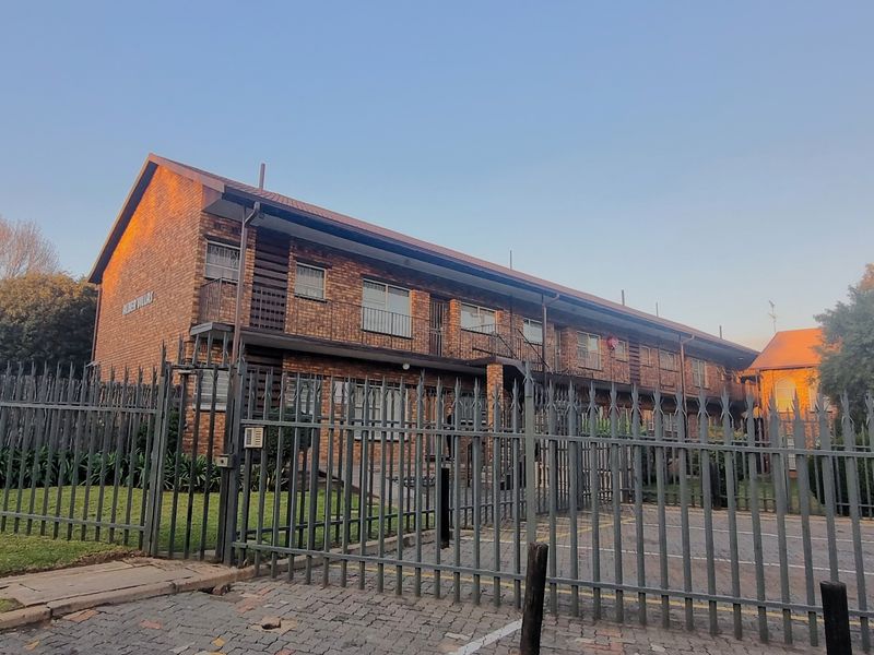 Exterior view of a multi-story face brick townhouse complex featuring secure metal perimeter fencing and a paved driveway entrance.