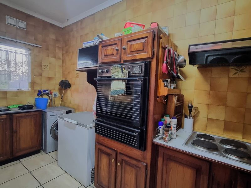A dated kitchen featuring wooden cabinetry, a built-in double oven, electric hob, extractor fan, and tiled splashbacks with a functional layout.