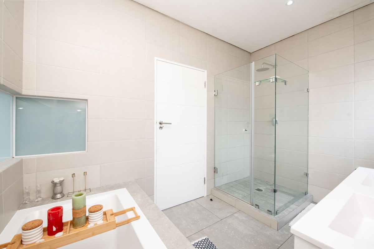 Modern bathroom featuring a glass-enclosed walk-in shower, a built-in bathtub, and neutral wall tiling.