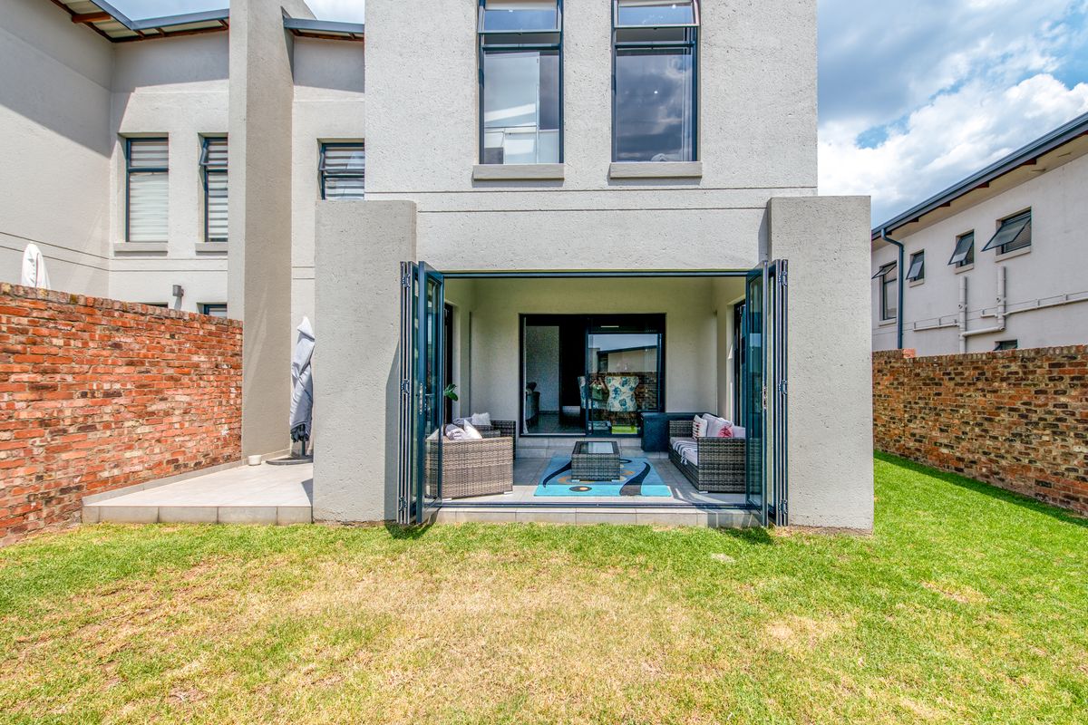 A rear view of the property featuring a covered patio with folding glass doors, leading to a private garden with brick boundary walls.