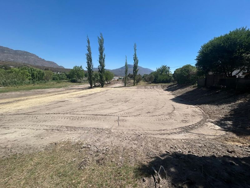 A wide-angle view of a vacant residential plot featuring cleared land, mature trees, and scenic mountain views in the background.