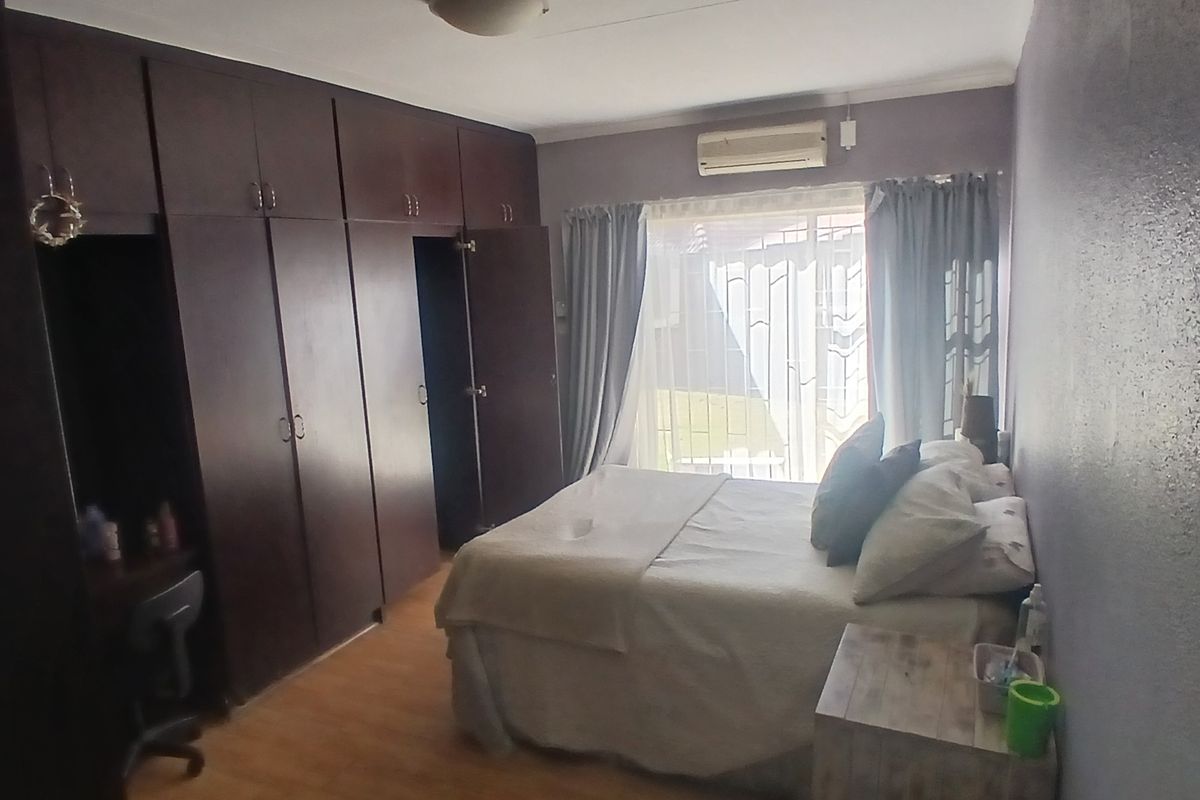 A bedroom featuring built-in dark wood cupboards, laminate flooring, and an integrated air conditioning unit with access to an outdoor area via a security gate.