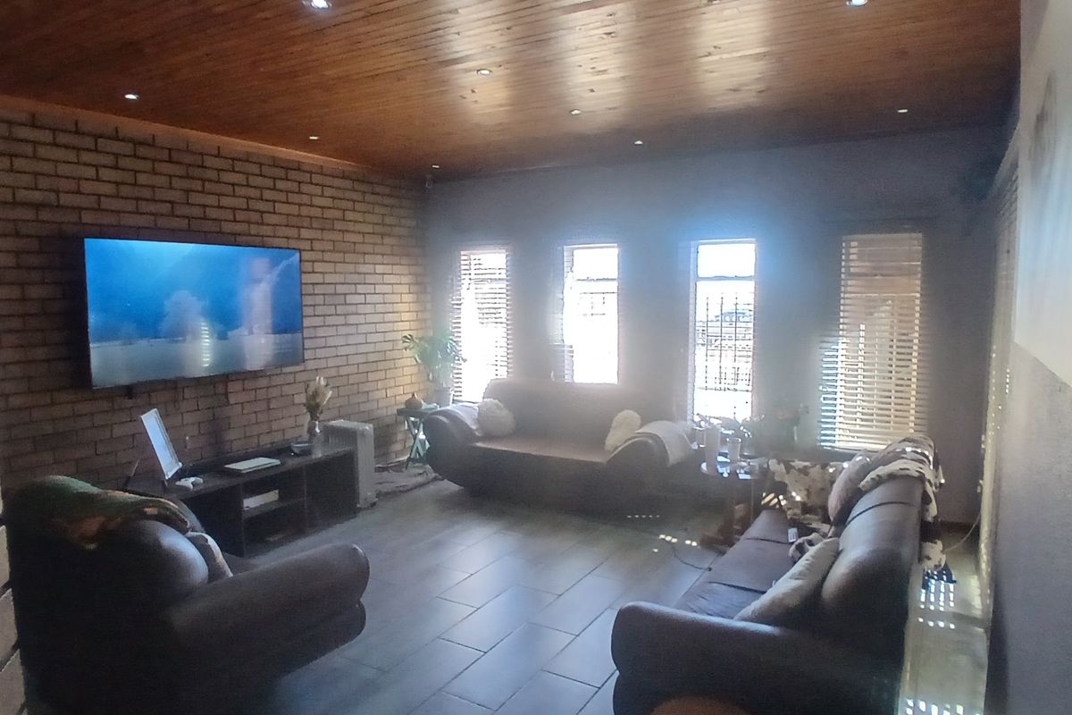 A living room featuring an exposed brick feature wall, timber ceiling with recessed lighting, and tiled flooring, providing a rustic and warm atmosphere.