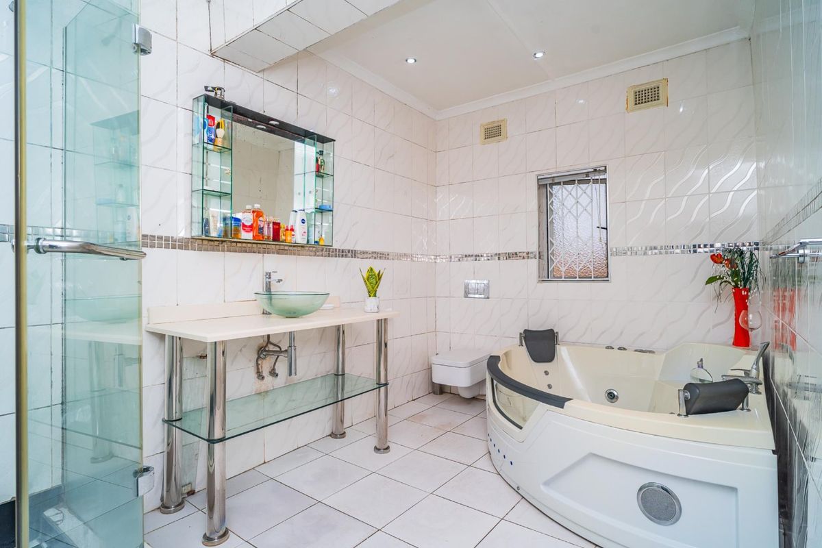 Spacious bathroom featuring a jetted corner bathtub, glass shower enclosure, wall-mounted toilet, and a modern glass vessel sink vanity.