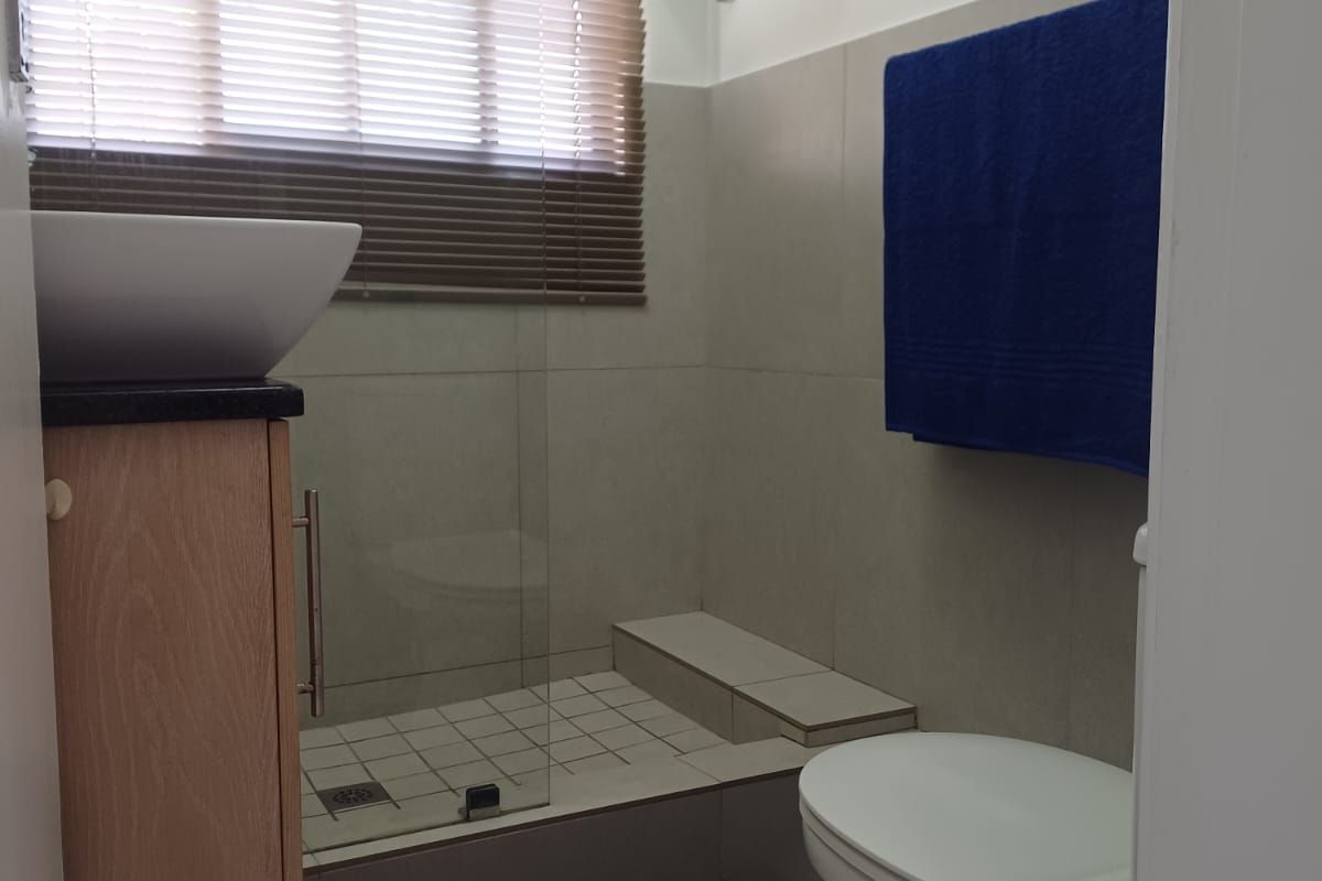 Compact bathroom featuring a vessel sink on a vanity cabinet, a glass-enclosed shower with tiled base, and a standard toilet.