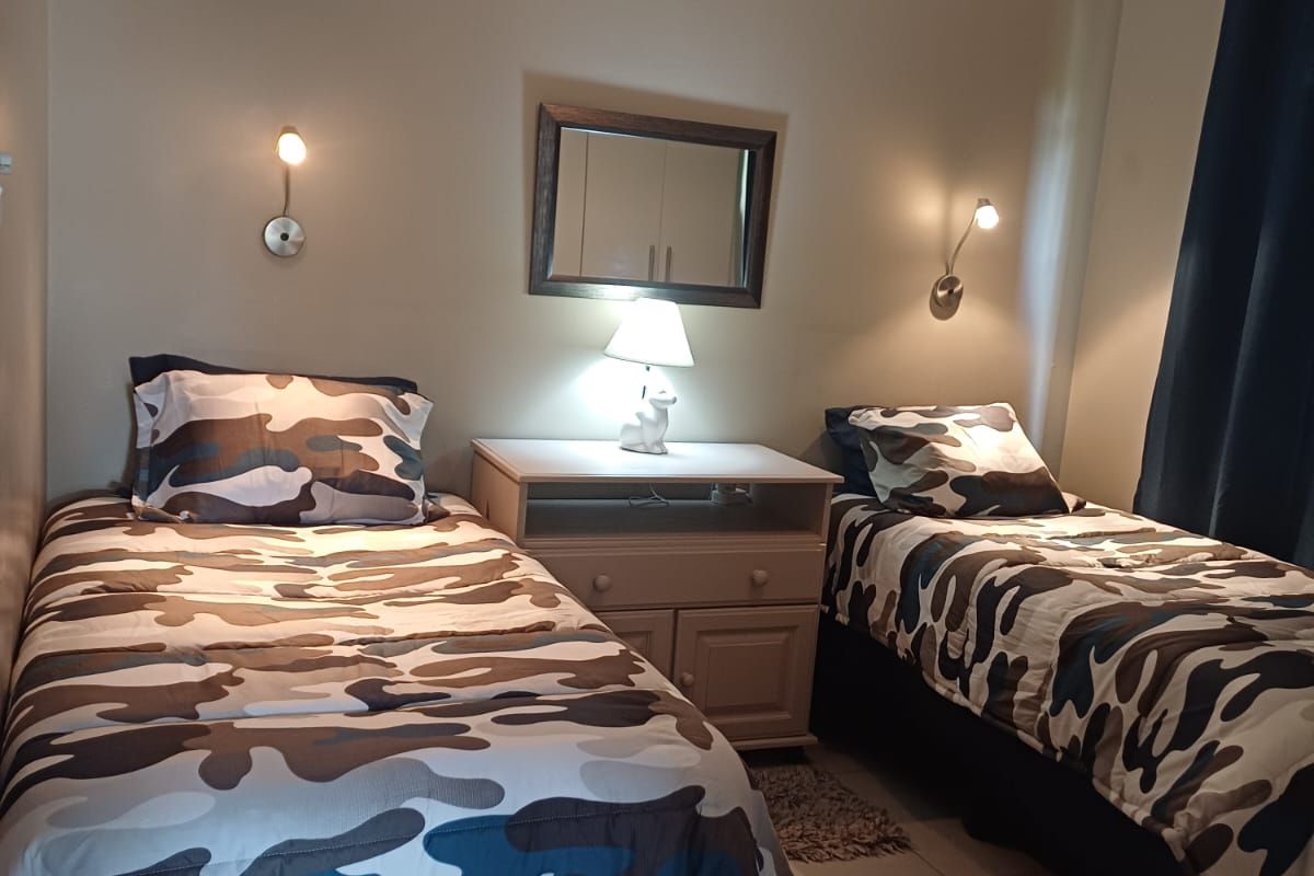 A bedroom featuring tiled flooring, a ceiling fan, and wall-mounted reading lights, providing a functional space for rest.