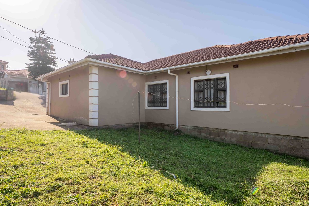 Rear exterior view of the house featuring a tiled roof, security bars on windows, and a grassed backyard area.