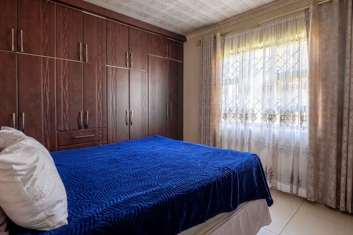 A bedroom featuring extensive dark wood built-in cupboards, tiled flooring, and a window fitted with security bars.