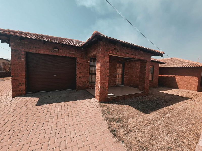 Front view of a face brick house featuring a tiled roof, a single roll-up garage, and a paved driveway with a covered entrance porch.