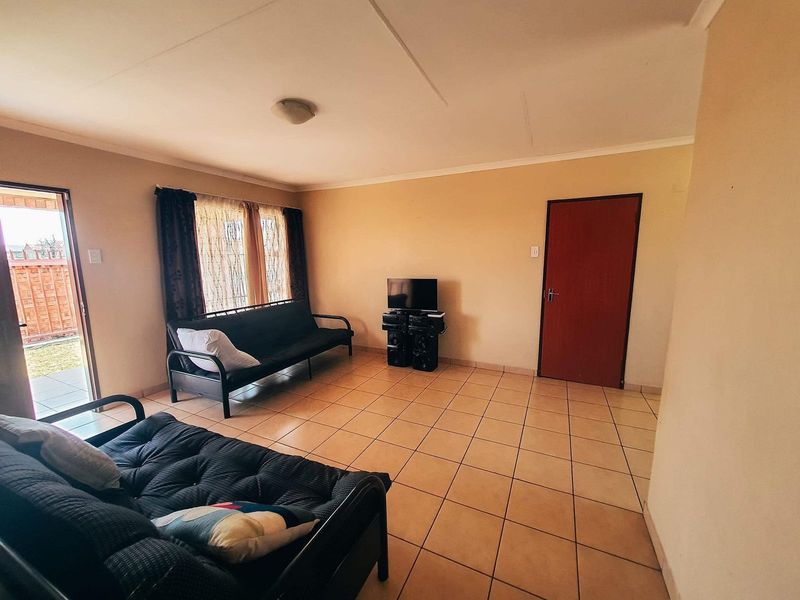 A simple living room featuring neutral wall tones, tiled flooring, and a sliding glass door providing access to the exterior.