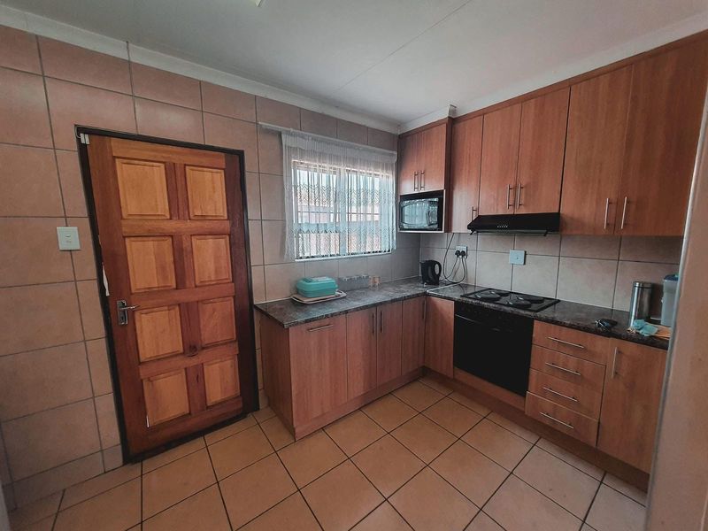 A functional kitchen featuring wood-finish cabinetry, tiled walls and flooring, a built-in oven with hob, and an integrated extractor fan.