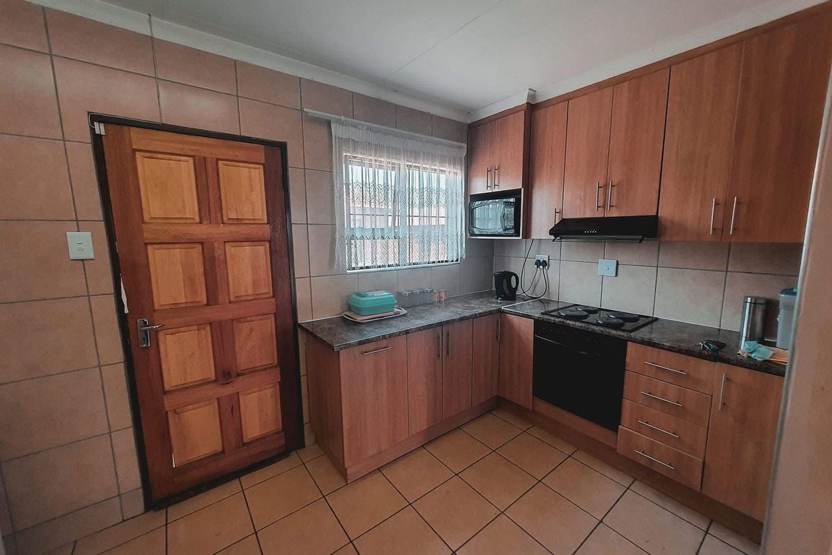 A functional kitchen featuring wood-finish cabinetry, tiled walls and flooring, a built-in oven with hob, and an integrated extractor fan.